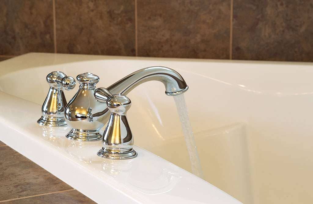 Closeup horizontal photo of chrome faucet running water into soaking tub in master bathroom