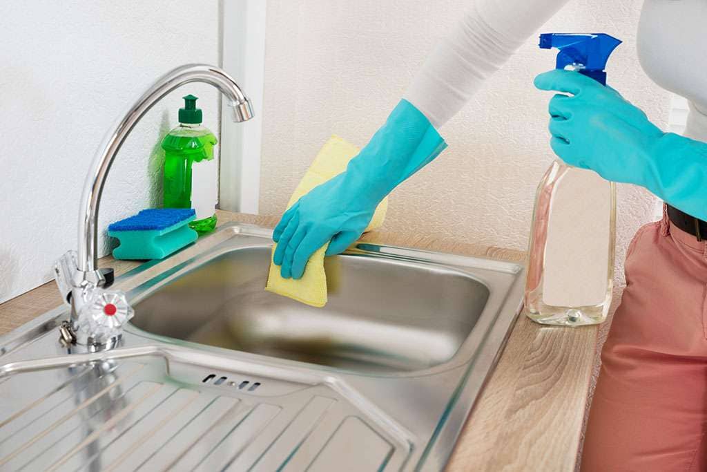 Close-up Of Woman Wiping Steel Kitchen Sink With Rag